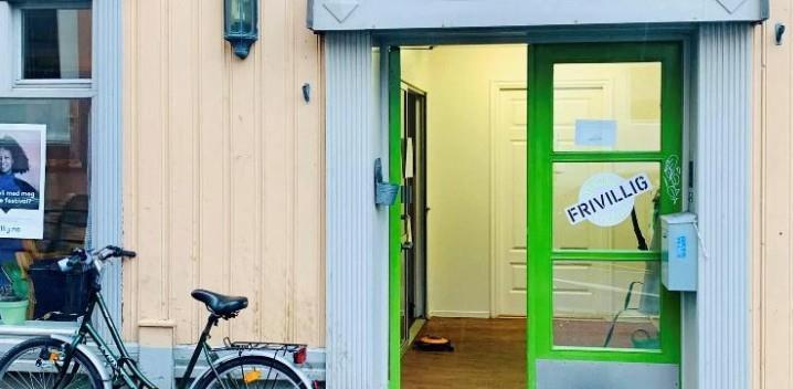 Inngangsparti med grønn dør der det står frivillig, og det står en sykkel utenfor. - Klikk for stort bilde