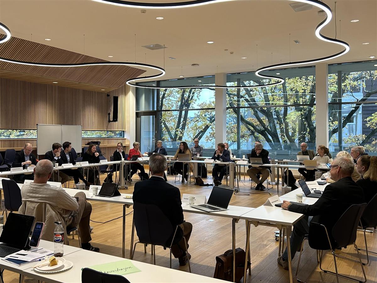 Oversiktsbilde av møtedeltakerne når de sitter ved bord i en stor firkant - Klikk for stort bilde