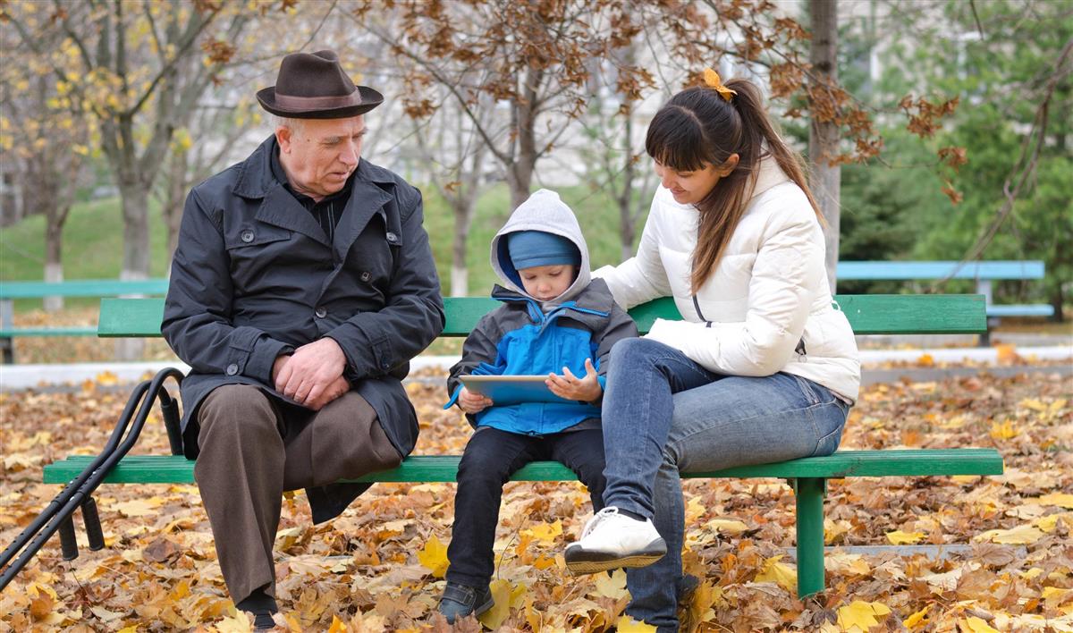 En eldre mann, et barn og en kvinne på en benk i en park.  - Klikk for stort bilde