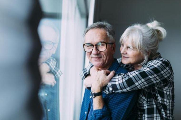 Eldre dame står bak en eldre mann og holder rundt han. - Klikk for stort bilde