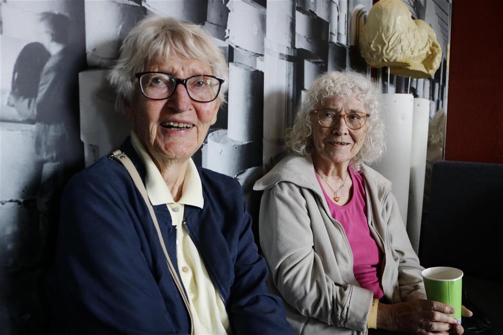 To eldre damer med grått hår og briller sitter og ser inn i kamera - Klikk for stort bilde