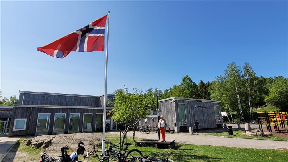 Flagg på flaggstang utenfor Røråstoppen skole. Rektor Anne Husby står ved siden av. - Klikk for stort bilde
