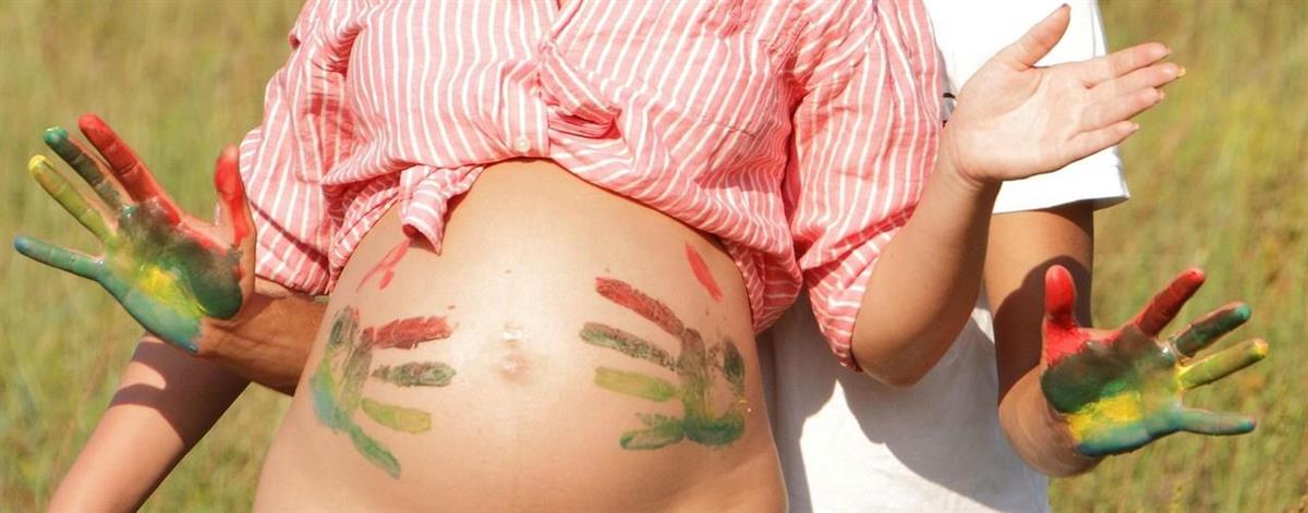 Bilde av en gravid mage og to hender som har maling på seg, som har tatt på magen. - Klikk for stort bilde