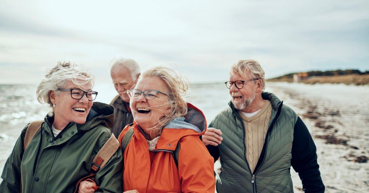 To blide middelaldrende damer og to menn står på stranden i turtøy - Klikk for stort bilde